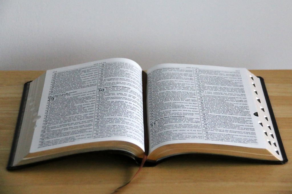 A close-up view of an open Bible on a wooden table, showcasing detailed text.
